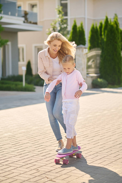 Mom helping her daughter ride a skateboard - Photo, Image