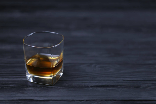 Glas mit Cognac- oder Whiskyalkoholgetränk auf schwarzem Holztisch in Großaufnahme mit Kopierraum für Text. Luxus-Elite-Alkoholkonsum oder Alkoholismus Konzept - Foto, Bild