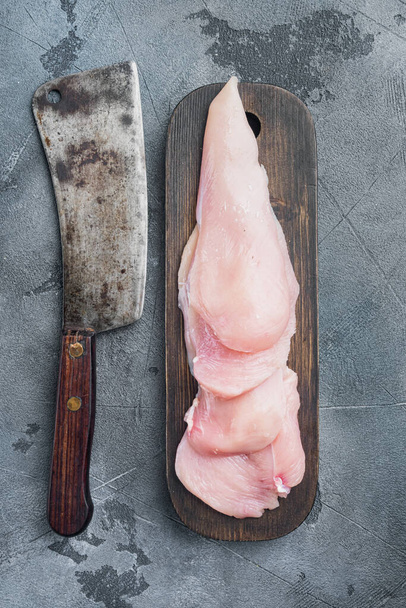Pieces of raw and uncooked chicken fillets, on gray background, top view flat lay - Foto, Imagem
