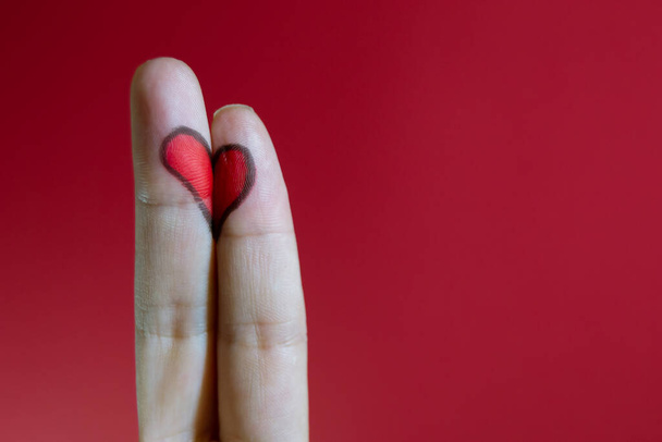 Das bemalte Herz auf weiblichen Fingern auf rotem Hintergrund. Valentinstag-Konzept. - Foto, Bild