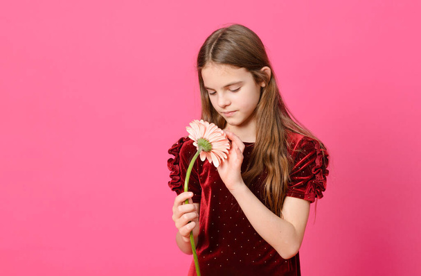 1 white teen girl with long hair in a red dress with a flower on a pink background - Foto, imagen