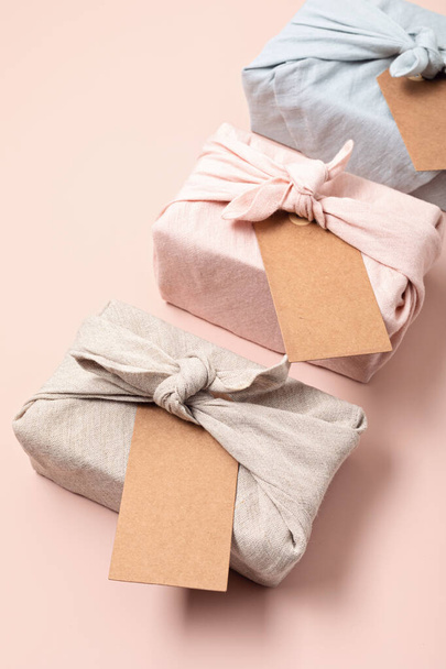 Zéró hulladék ajándék csomagolás hagyományos japán furoshiki stílus rózsaszín háttér. Műanyag ingyenes, kézzel készített ajándék csomag karácsonyra, születésnapra, húsvétra és egyéb ünnepi alkalmakra - Fotó, kép