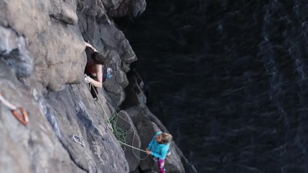 Ένα κορίτσι σκαρφαλώνει ένα βράχο πάνω από το νερό - Πλάνα, βίντεο