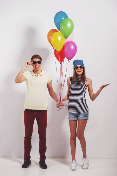 Piękna para stoją na szarym tle, trzymając kolorowe balony i uśmiechnięty do aparatu. - Zdjęcie, obraz