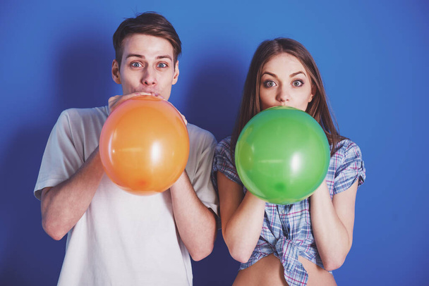 Cheerful couple having fun together. They are inflating balloons on blue background. - Foto, immagini