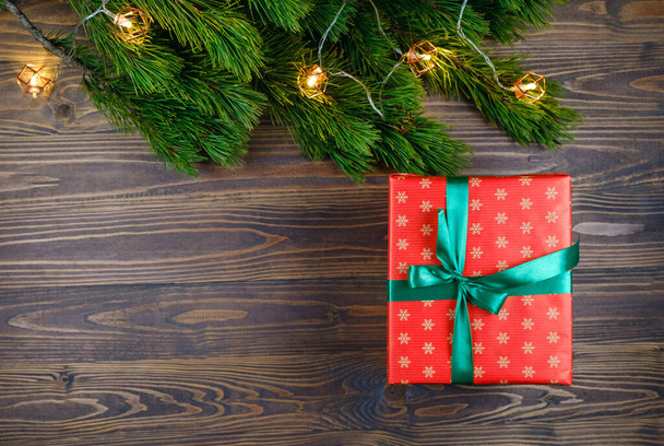 Caja de regalo de Navidad sobre fondo de madera con rama de árbol de Navidad y luces. Tema Navidad y Feliz Año Nuevo. Asiento plano, vista superior. Copiar espacio - Foto, Imagen