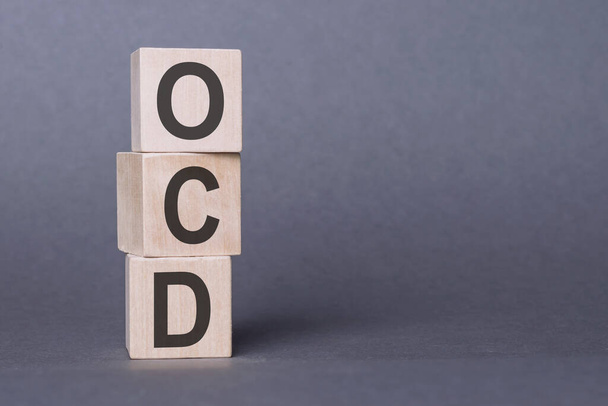 OCD - Zwangsstörung, Text, geschrieben auf Holzklötzen, auf grauem Hintergrund. - Foto, Bild