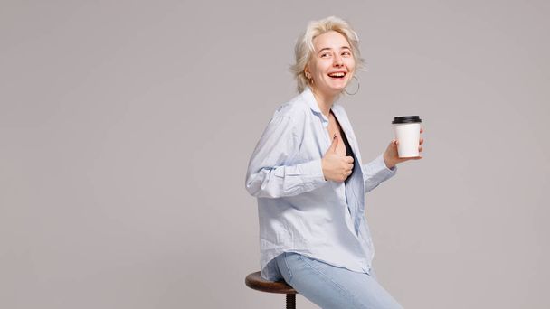 Блондинка держит пластиковую чашку с напитком в руках на светлом фоне - Фото, изображение