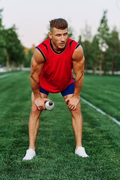 Cheerful sporty man in the park on green grass doing exercises - Photo, image