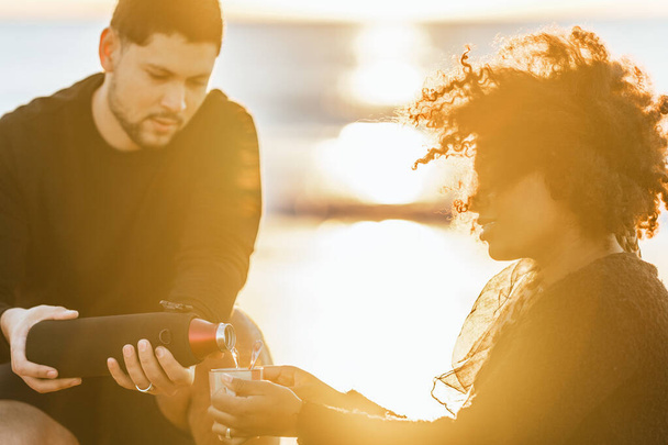 Pôr do sol iluminando um homem que serve chá para uma mulher sentada na praia - Foto, Imagem