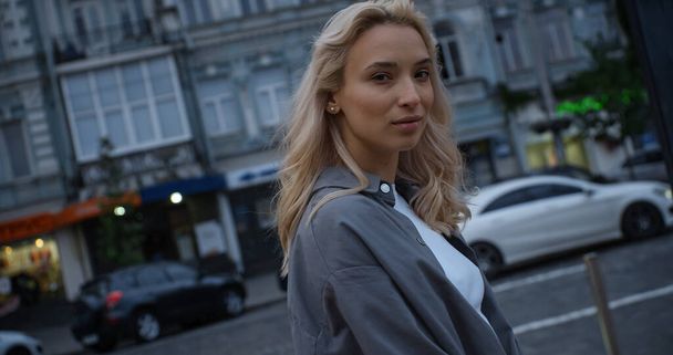 Blonde female model walking in evening city near road with driving cars. - Photo, Image
