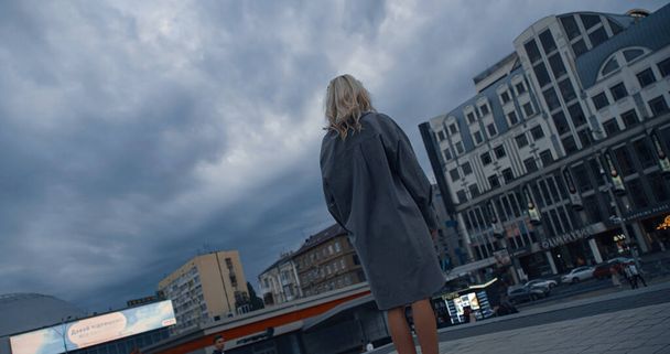 Blondine vrouw staande gebouwen op regenachtige stad 's avonds stedelijk gebied.  - Foto, afbeelding
