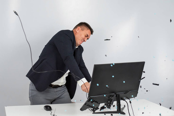 Caucasian man in a suit gets angry and smashes the keyboard on the monitor. An office worker in a rage breaks the computer. - Фото, изображение
