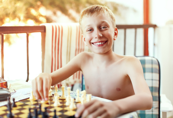 Beautiful little boy sitting in chair outdoors on summer vacation playing chess - Photo, Image