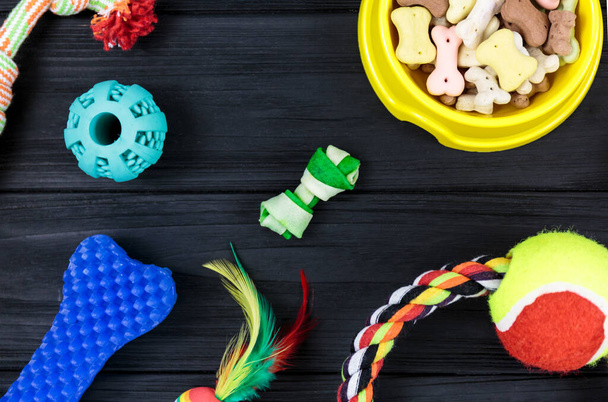 Different accessories for dogs and cats: mouse toy, ball, comb, leash, collar, toys and bowl with bones on black wooden background. Pets care and routine concept. close up, top view - Photo, image