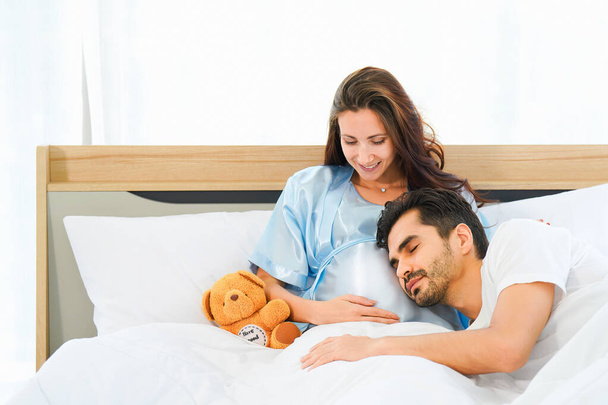 portrait of happy pregnant wife and husband lying together on bed in bed room at home - Фото, изображение