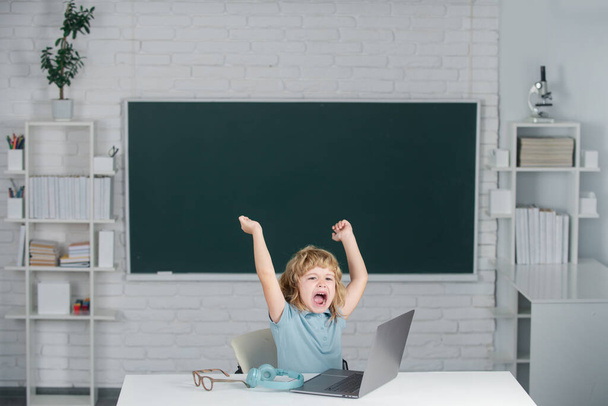 Angry sad screaming kid boy shouting on lesson at school, making homework and using notebook gadget. Bad school boy. - 写真・画像