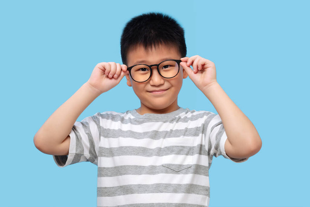 眼鏡とTシャツを身に着けて青い背景で視力検査を受ける子供 - 写真・画像