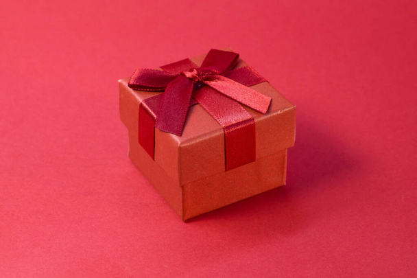 Закрытая красная подарочная коробка с шелковой золотой лентой бант на ярко-розовом фоне - Фото, изображение
