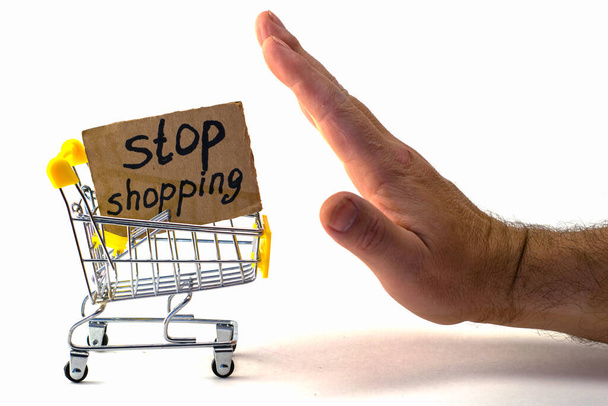 kohtuullisen kulutuksen ostamisesta luopuminen henkilö työntää ostoskärryä merkillä, jossa on merkintä lopeta ostokset valkoisella taustalla kädellään. Laadukas kuva - Valokuva, kuva