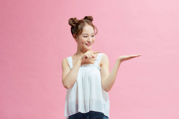 Lady holding palm up and pointing to her right while looking at you smiling in pink background - Foto, imagen