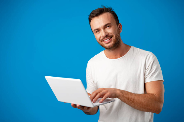 Handsome young man using his laptop against blue background - Foto, imagen