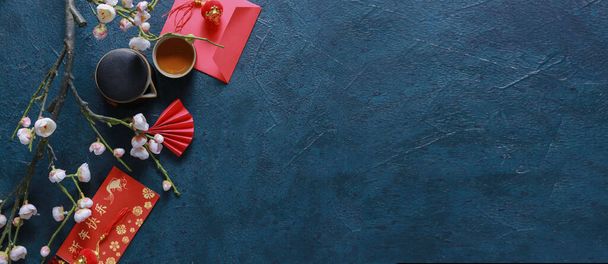 Tradycyjna chińska herbata z czerwonymi kopertami i kwitnącymi gałęziami śliwki na ciemnym tle z miejscem na tekst - Zdjęcie, obraz