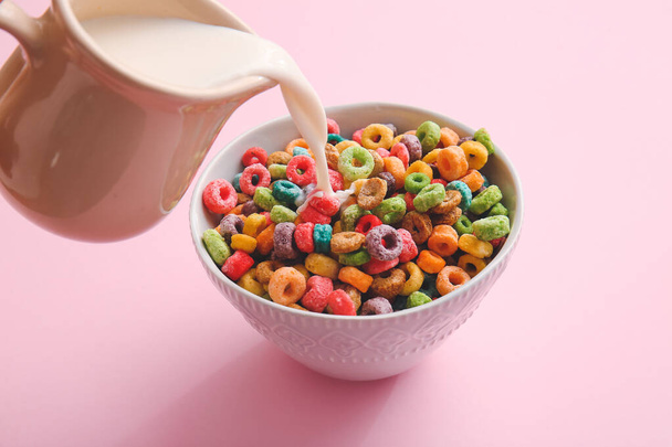 Pouring milk in bowl of colorful cereal rings on pink background - Foto, afbeelding