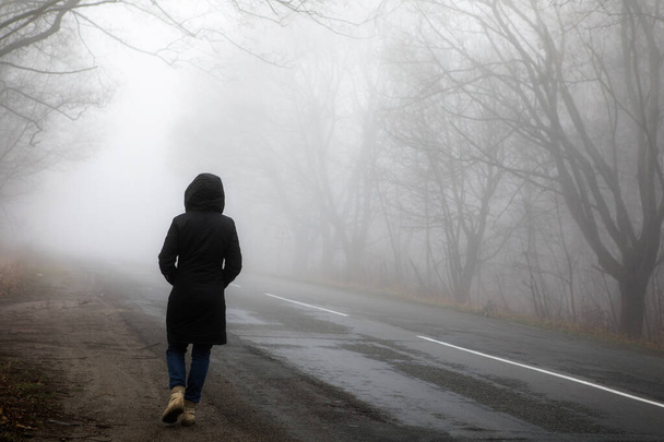 Nebellandschaft. Frau läuft allein auf beängstigend nebliger Straße. - Foto, Bild