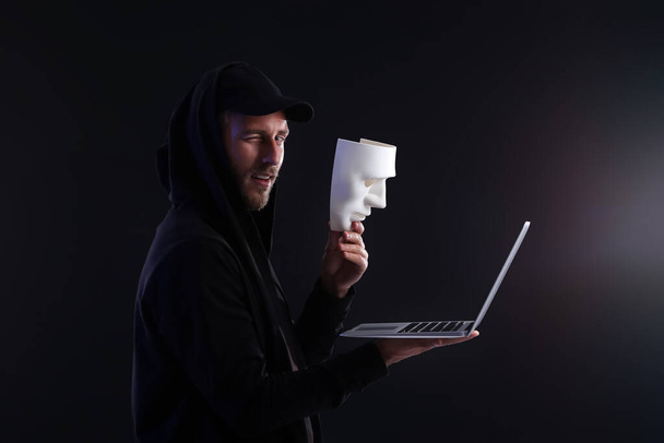 Hacker με laptop και μάσκα σε σκούρο φόντο - Φωτογραφία, εικόνα