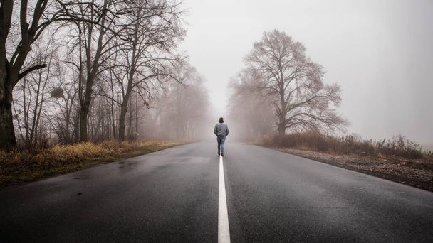 男だけが離れて劇的な神秘的なシーンで霧霧の霧の道に歩いてください。男は霧に包まれた秋の風景の中を歩く - 写真・画像