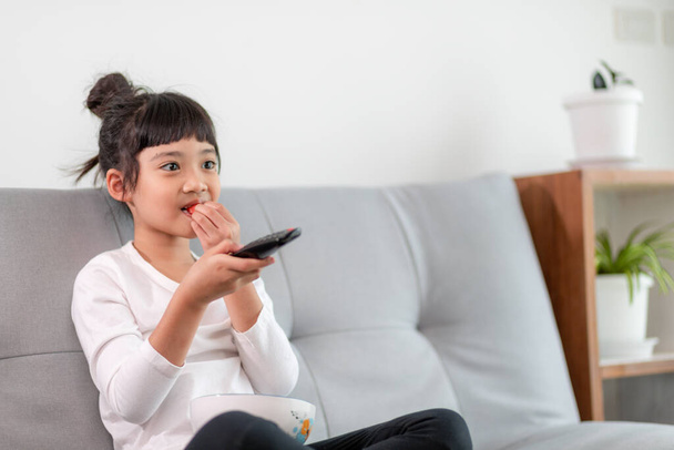 Criança com controle remoto sentado no sofá assistindo a um filme na TV - Foto, Imagem