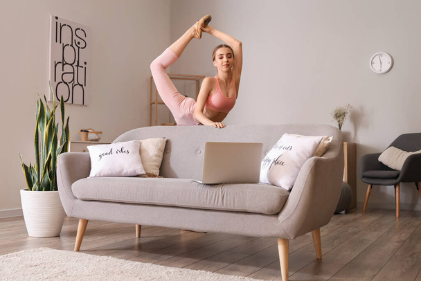 Dizüstü bilgisayarlı güzel bir kadın evde jimnastik yapıyor. - Fotoğraf, Görsel