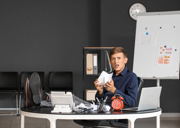 Нещасний молодий бізнесмен зі збитим паперовим листом, сидячи за столом в офісі
 - Фото, зображення