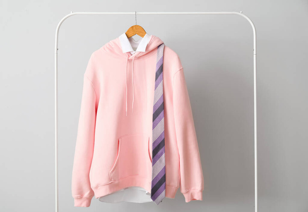 Rack met stijlvolle roze hoodie, shirt en stropdas bij lichte wand - Foto, afbeelding