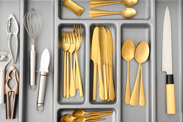 Open kitchen drawer with golden cutlery and utensils, closeup - Photo, Image