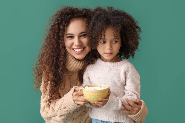 klein Afro-Amerikaans meisje en haar moeder met mok van cacao op groene achtergrond - Foto, afbeelding