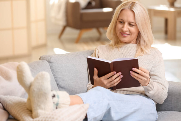 Beautiful mature woman reading book at home on autumn day - Photo, Image