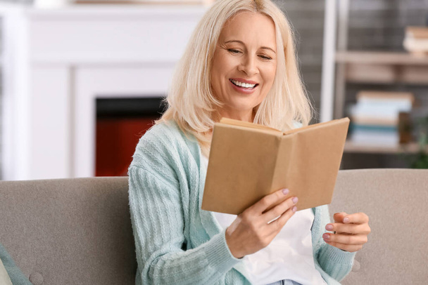 Hermosa mujer madura leyendo libro en casa en el día de otoño - Foto, Imagen