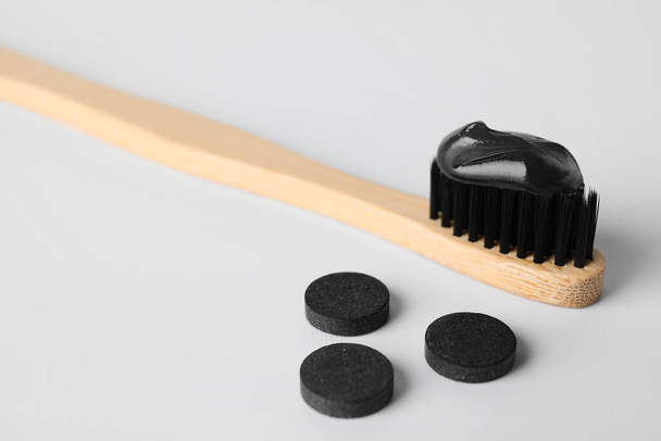 Brosse en bambou avec de la pâte dentaire noire et des pilules de charbon actif sur fond blanc - Photo, image