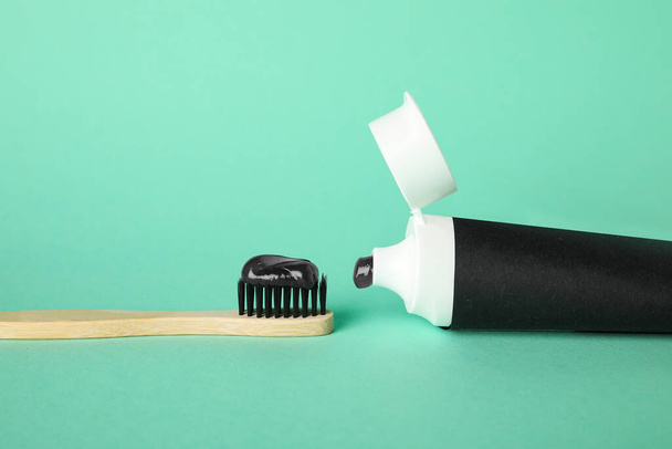 Трубка с черной зубной пастой и бамбуковой щеткой на зеленом фоне - Фото, изображение