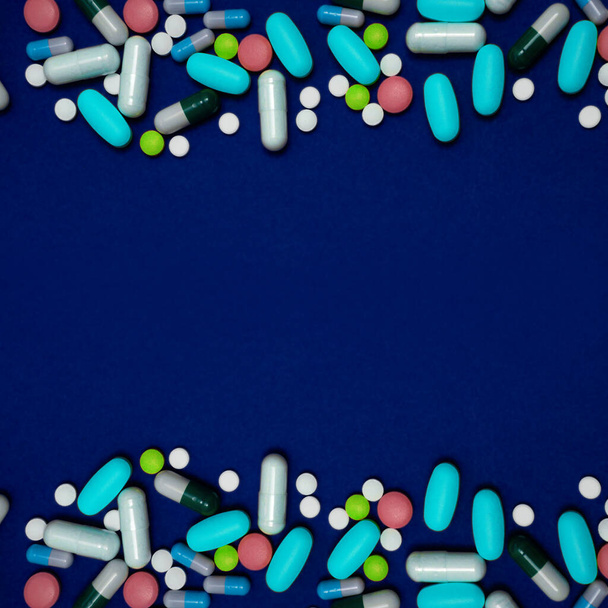 Синий фон с копировальным пространством и множеством лекарств в капсулах и таблетках разных цветов, разбросанных по поверхности - Фото, изображение