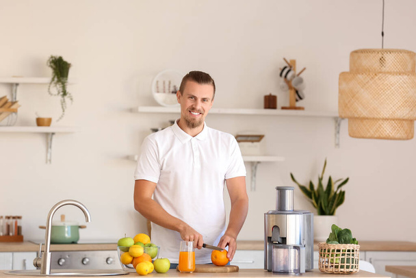 Young man preparing healthy fruit juice in kitchen - Zdjęcie, obraz