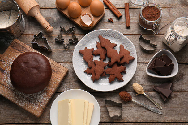 Plate with tasty chocolate Christmas cookies, dough and ingredients on wooden background - Photo, Image