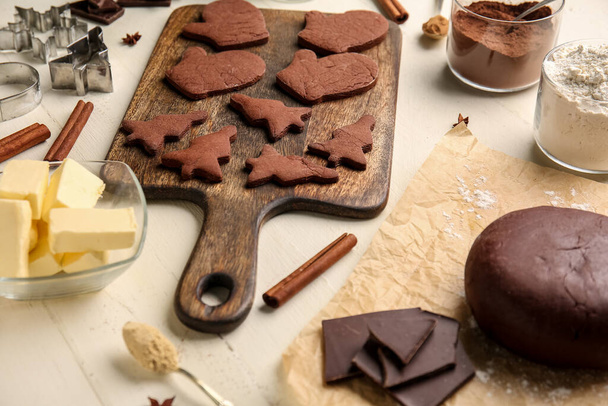 Board with tasty chocolate Christmas cookies and ingredients on white wooden background - Photo, Image