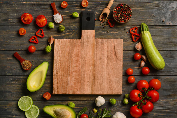 Dřevěná řezací deska s chutným jídlem a kořením na tmavém pozadí - Fotografie, Obrázek