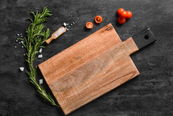 Wooden cutting board with tomatoes, sea salt and rosemary on dark background - Photo, Image