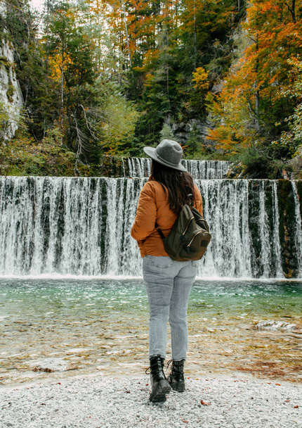A Caucasian woman with autumn clothes standing in front of the waterfall in Kranjska Gora, Slovenia - Foto, Imagen