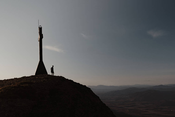 Uma pessoa silhueta em pé no topo de uma montanha em frente a uma cruz - Foto, Imagem