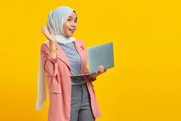 привлекательная молодая азиатка улыбается держа в руках ноутбук и приветствие - Фото, изображение